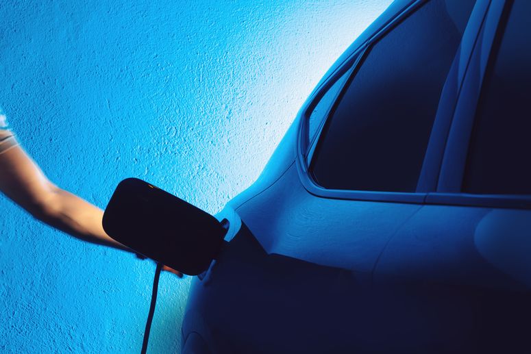 Una persona está enchufando un vehículo eléctrico para cargarlo en un aparcamiento privado, con la escena iluminada dramáticamente en tonos azules.